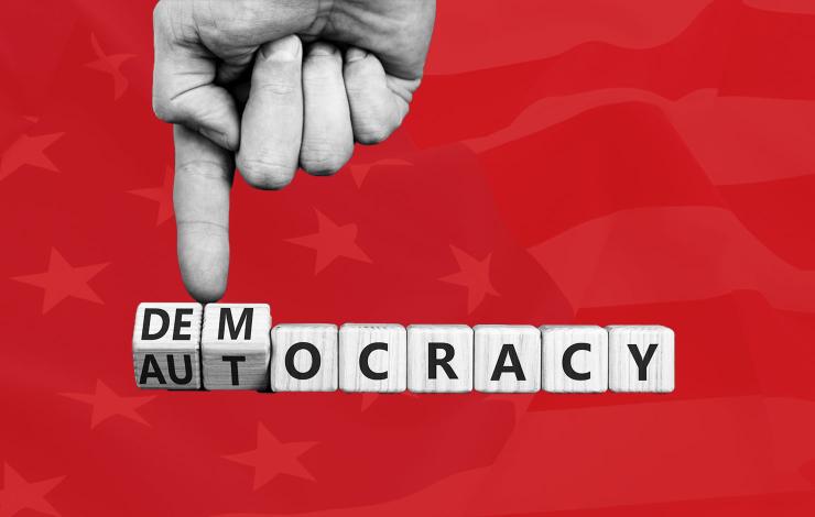 A finger pushing back against blocks that say "autocracy" so that they say "democracy"