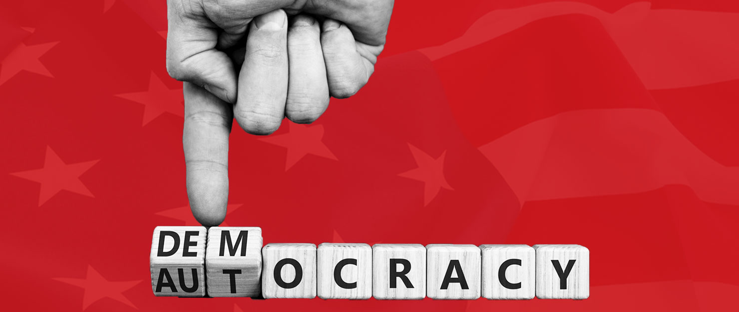 Hand pushing back against the word "autocracy" so that it says "democracy"