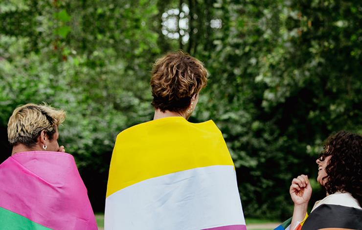 Three people wearing pride flags over their shoulders reflecting a diversity of LGBTQ+ identities 